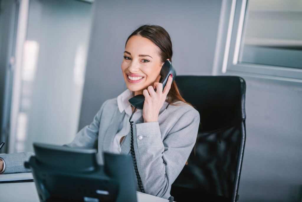 Eine Frau lächelt mit einem Telefonhörer am Ohr in die Kamera.